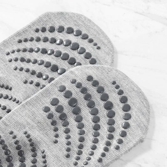 Close-up of the sole of a pair of grey non-slip yoga or Pilates socks. The image clearly showcases the pattern and size of the dark grey rubber grip dots used for maximum traction on the floor.