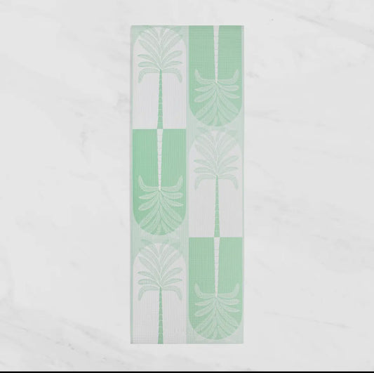 An overhead view of a mint green and white patterned yoga or fitness towel, featuring a repeated design of palm fronds and arches. The towel is laid flat on a white marble-style background.