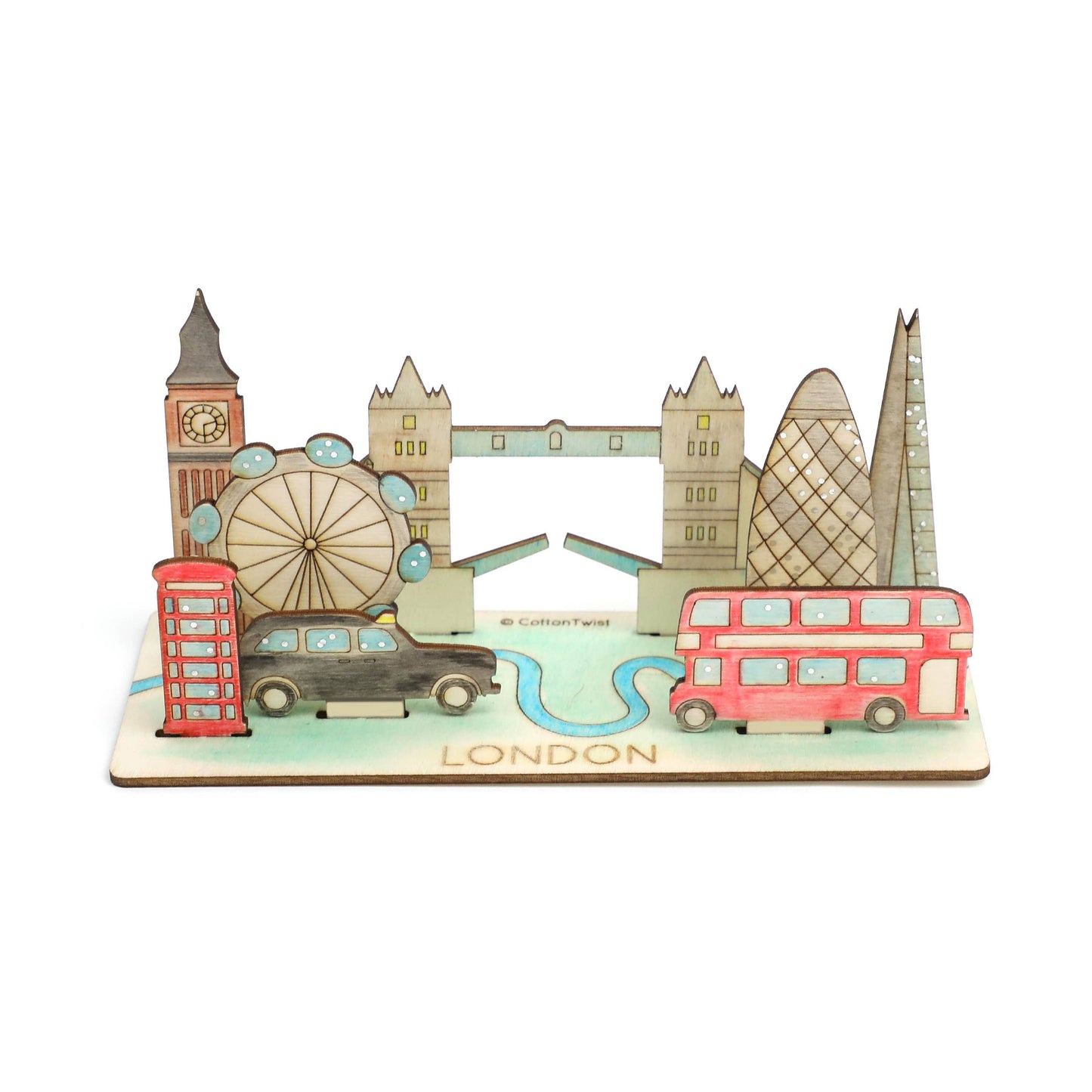 The fully assembled and hand-colored wooden 3D London model on a white background. The finished scene features iconic landmarks, including Tower Bridge, Big Ben, the London Eye, the Gherkin, a double-decker bus, a taxi, and a red phone booth, on a base labeled 'LONDON.'