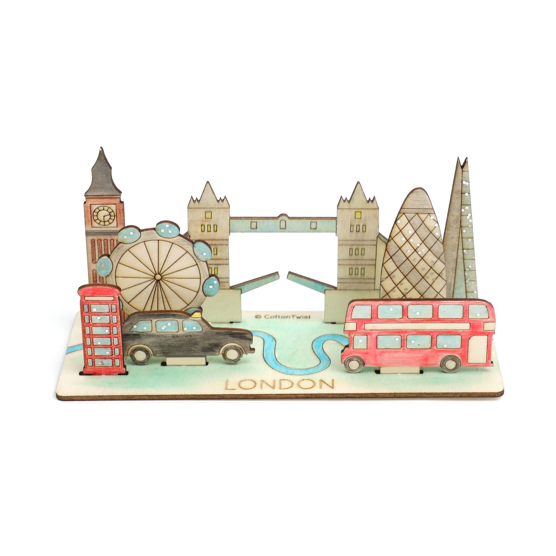 The fully assembled and hand-colored wooden 3D London model on a white background. The finished scene features iconic landmarks, including Tower Bridge, Big Ben, the London Eye, the Gherkin, a double-decker bus, a taxi, and a red phone booth, on a base labeled 'LONDON.'