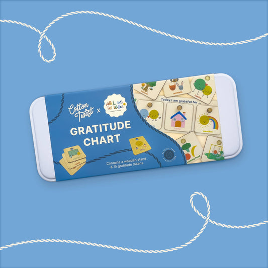 Retail packaging for the 'Cotton Twist x ABL Long Live The Lab' Gratitude Chart craft kit. The blue box shows the wooden stand and several feeling tokens, confirming it 'Contains a wooden stand & 16 feeling tokens,' with illustrations for Home, Family, and Rainbow visible.