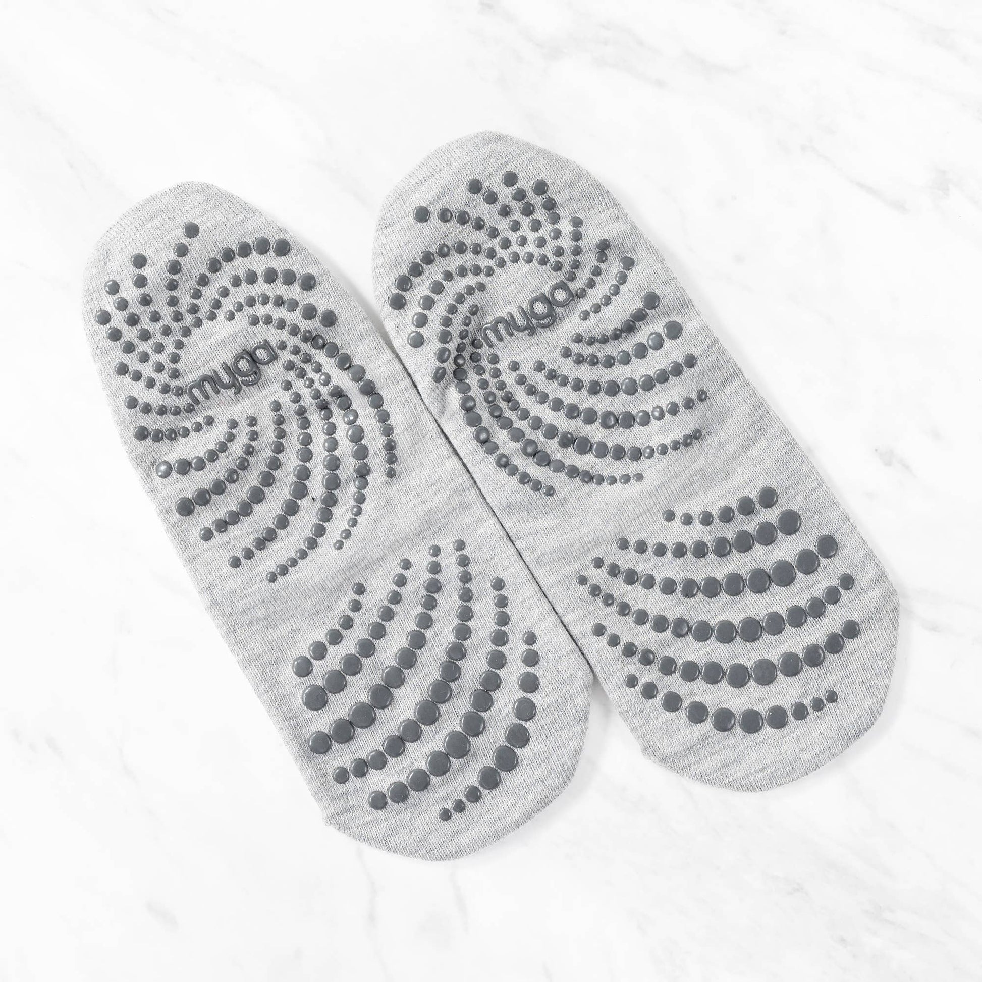 Overhead view of a pair of grey non-slip yoga or barre socks laid out, showing the entire sole. The soles feature a distinct swirling pattern of dark grey grip dots to ensure maximum traction and stability during floor work.