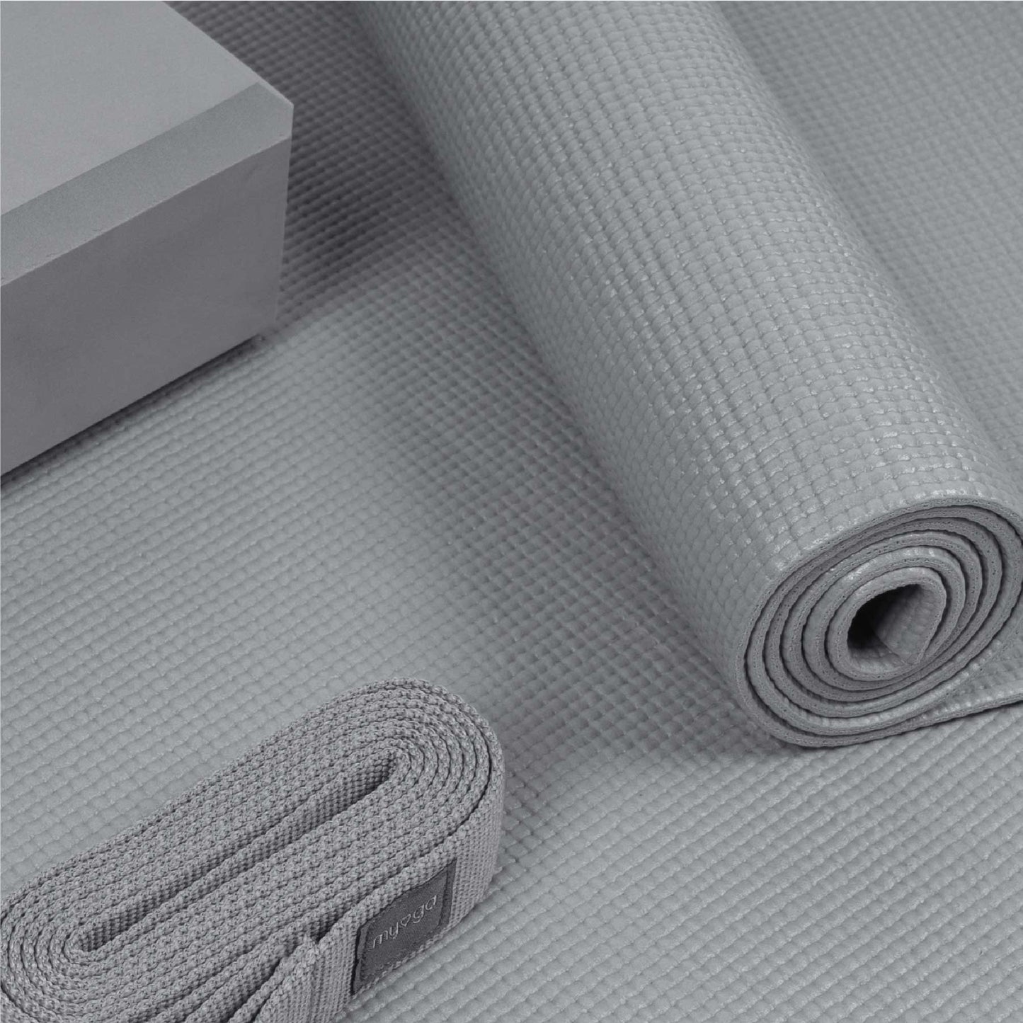 Close-up of a grey Myga yoga set showing the texture of the rolled yoga mat. Also visible are the matching foam yoga block and the yoga strap, highlighting the quality of the yoga accessories.