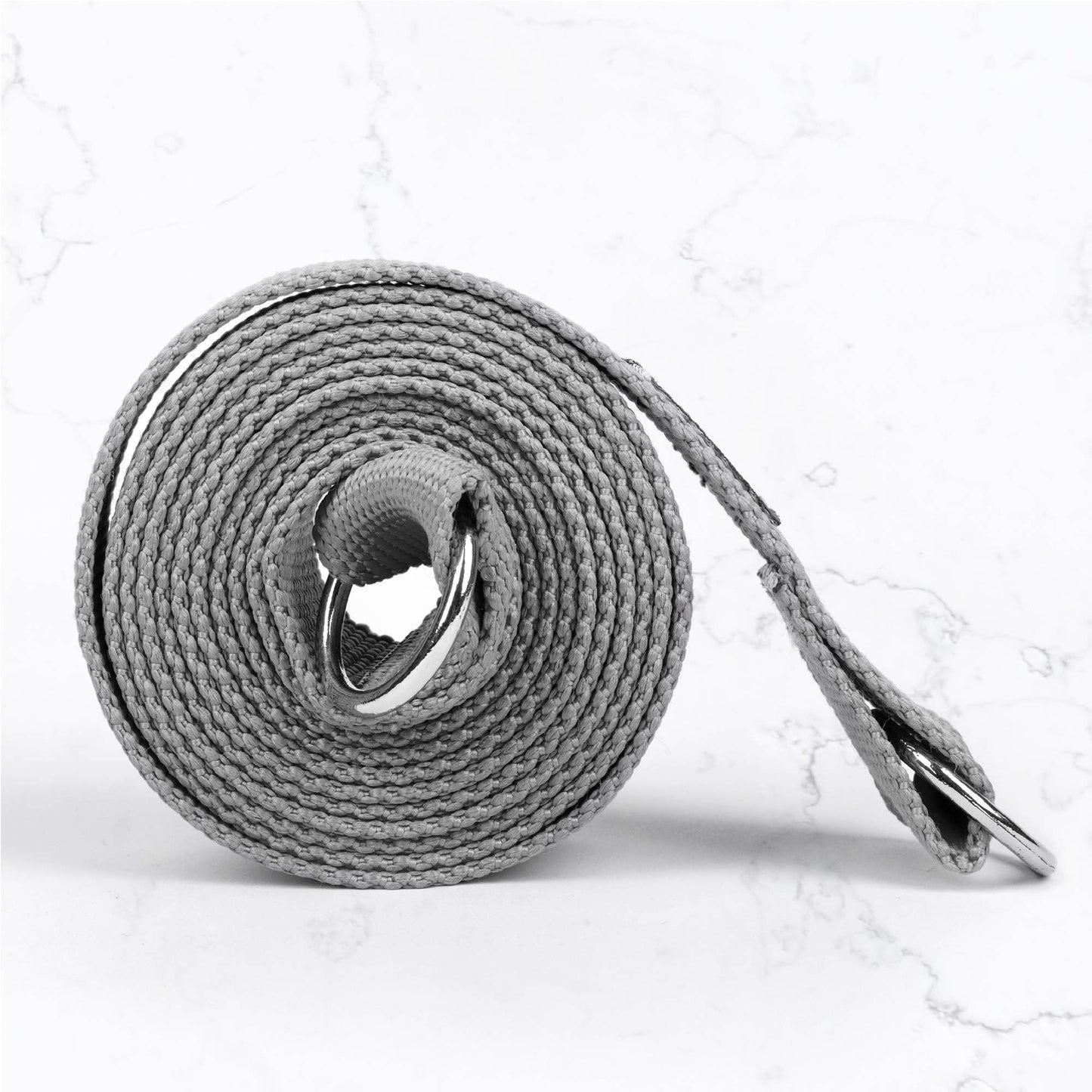 Close-up of a tightly rolled grey cotton yoga strap with silver D-rings for adjusting the length, highlighting the texture and hardware of the yoga accessory.