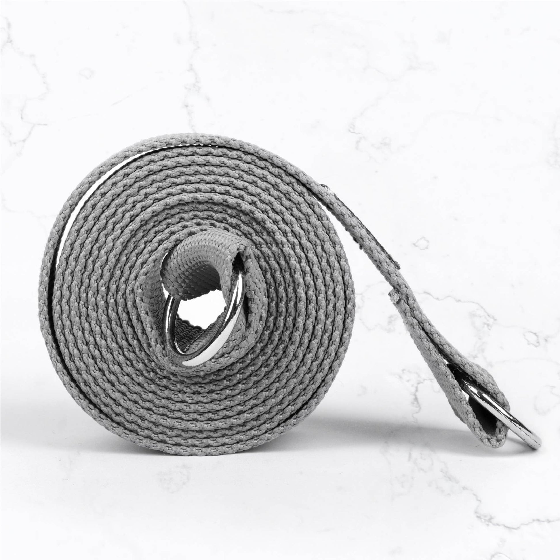 Close-up of a tightly rolled grey cotton yoga strap with silver D-rings for adjusting the length, highlighting the texture and hardware of the yoga accessory.