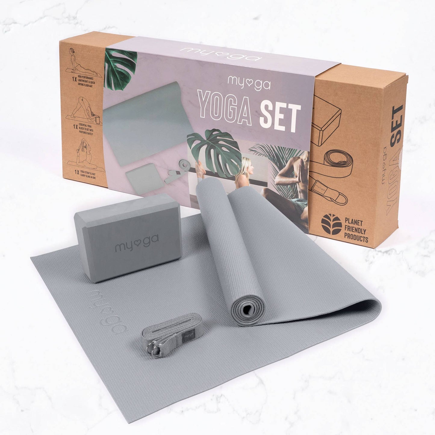 The Myga 3-piece Yoga Set in grey is displayed on a marble-style floor in front of its cardboard retail box. The set includes a rolled yoga mat, a foam yoga block, and a matching yoga strap, highlighting a complete kit for yoga or fitness practice.