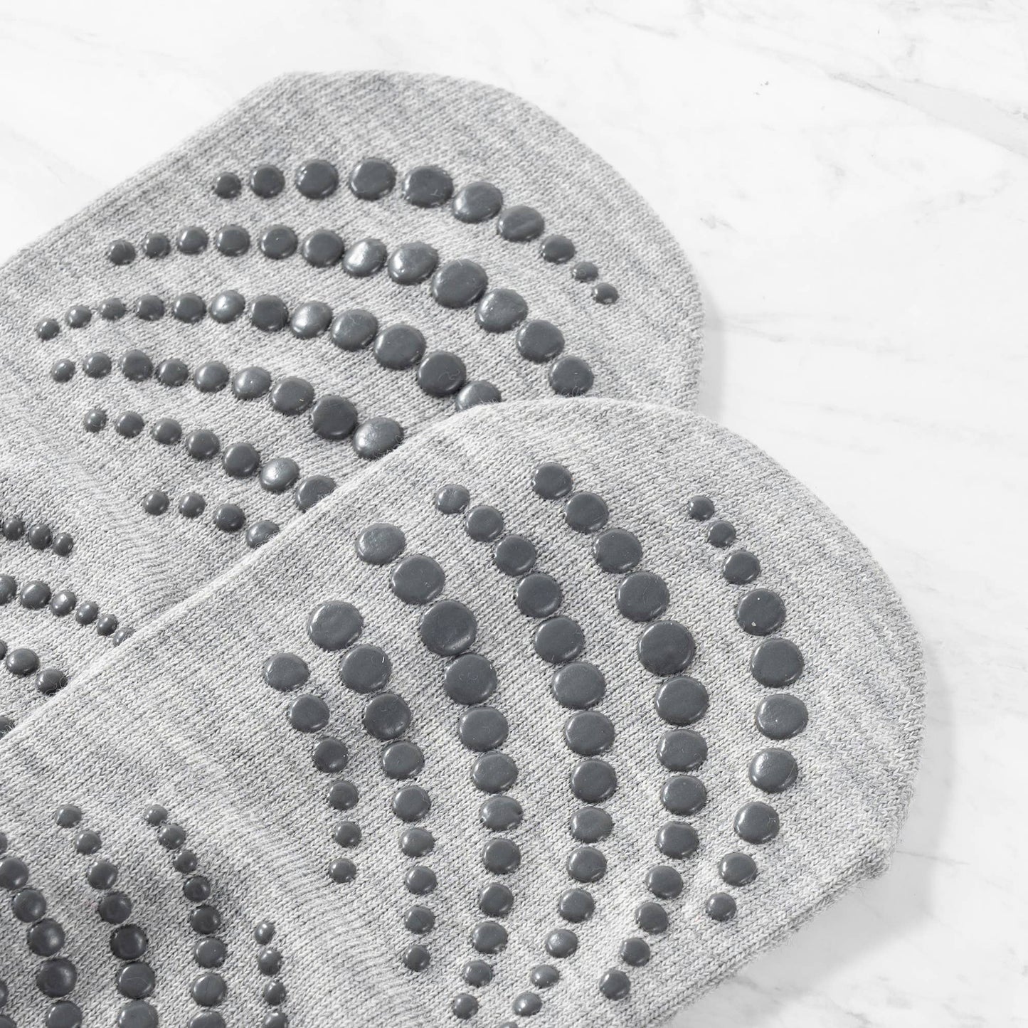 Close-up of the sole of a pair of grey non-slip yoga or Pilates socks. The image clearly showcases the pattern and size of the dark grey rubber grip dots used for maximum traction on the floor.