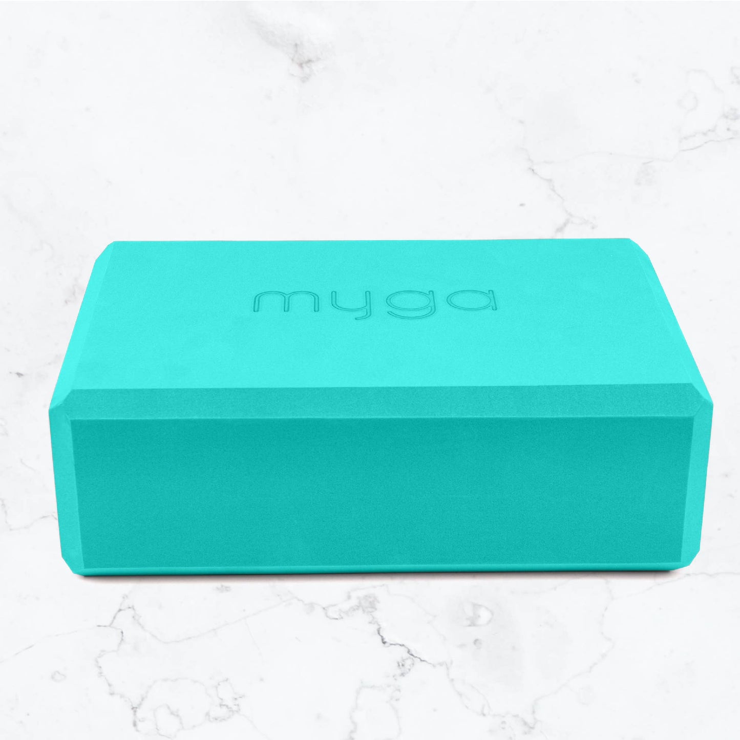 Turquoise yoga block with 'myga' branding on a white marble background