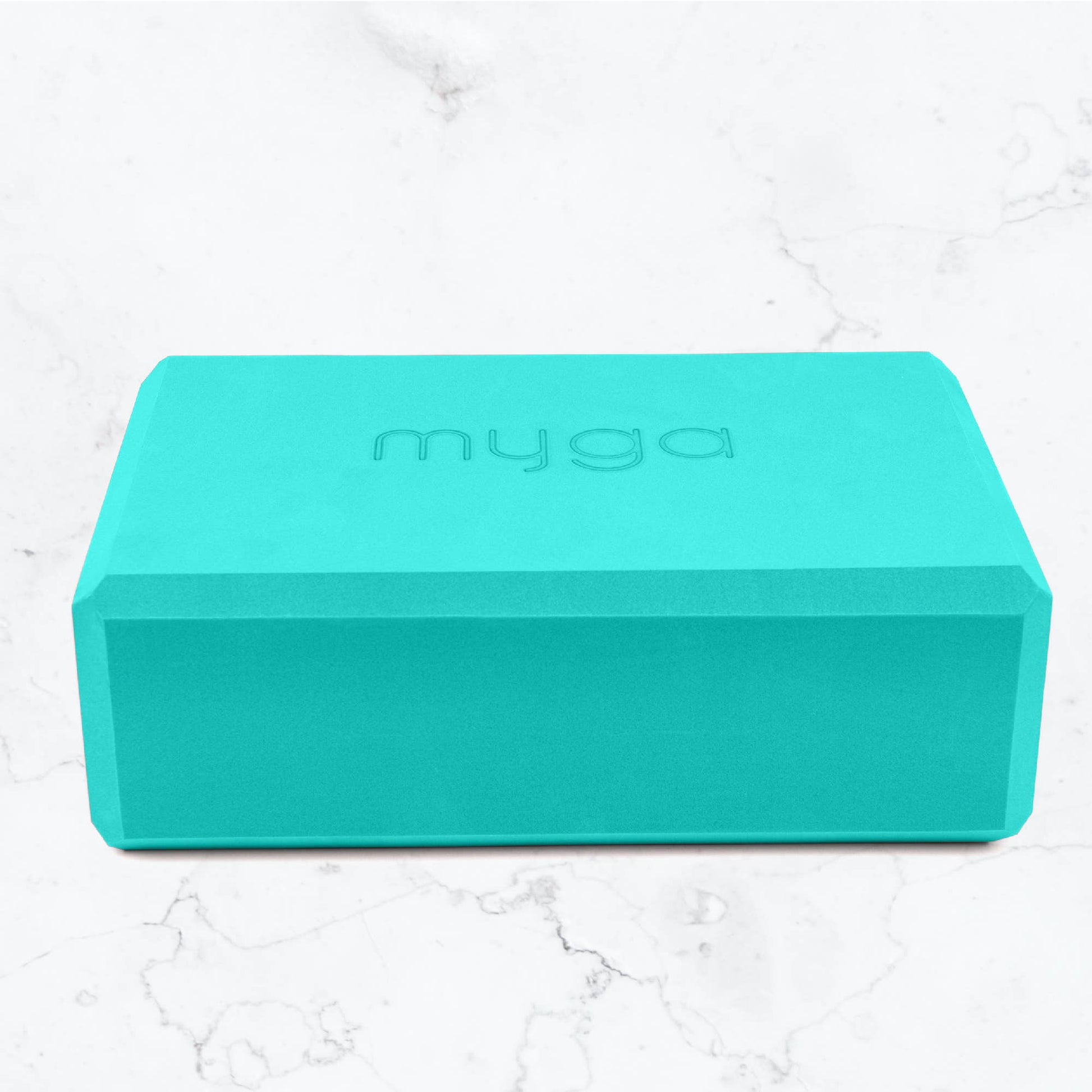 Turquoise yoga block with 'myga' branding on a white marble background