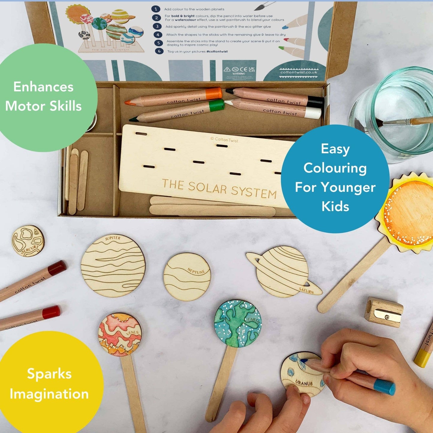 Marketing graphic showing a child coloring a planet from the DIY Solar System craft kit, highlighting the product benefits: Enhances Motor Skills, Easy Colouring for Younger Kids, and Sparks Imagination. The open kit box and wooden stand are visible in the background.