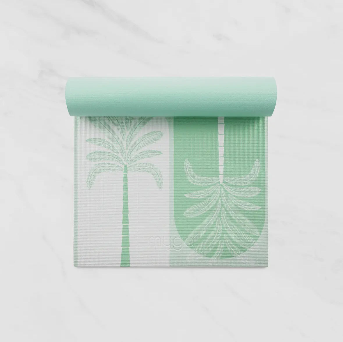 An overhead view of a partially rolled mint green and white Myga yoga mat featuring a distinct, repeating palm tree pattern. The mat is laid out on a white marble-style background.