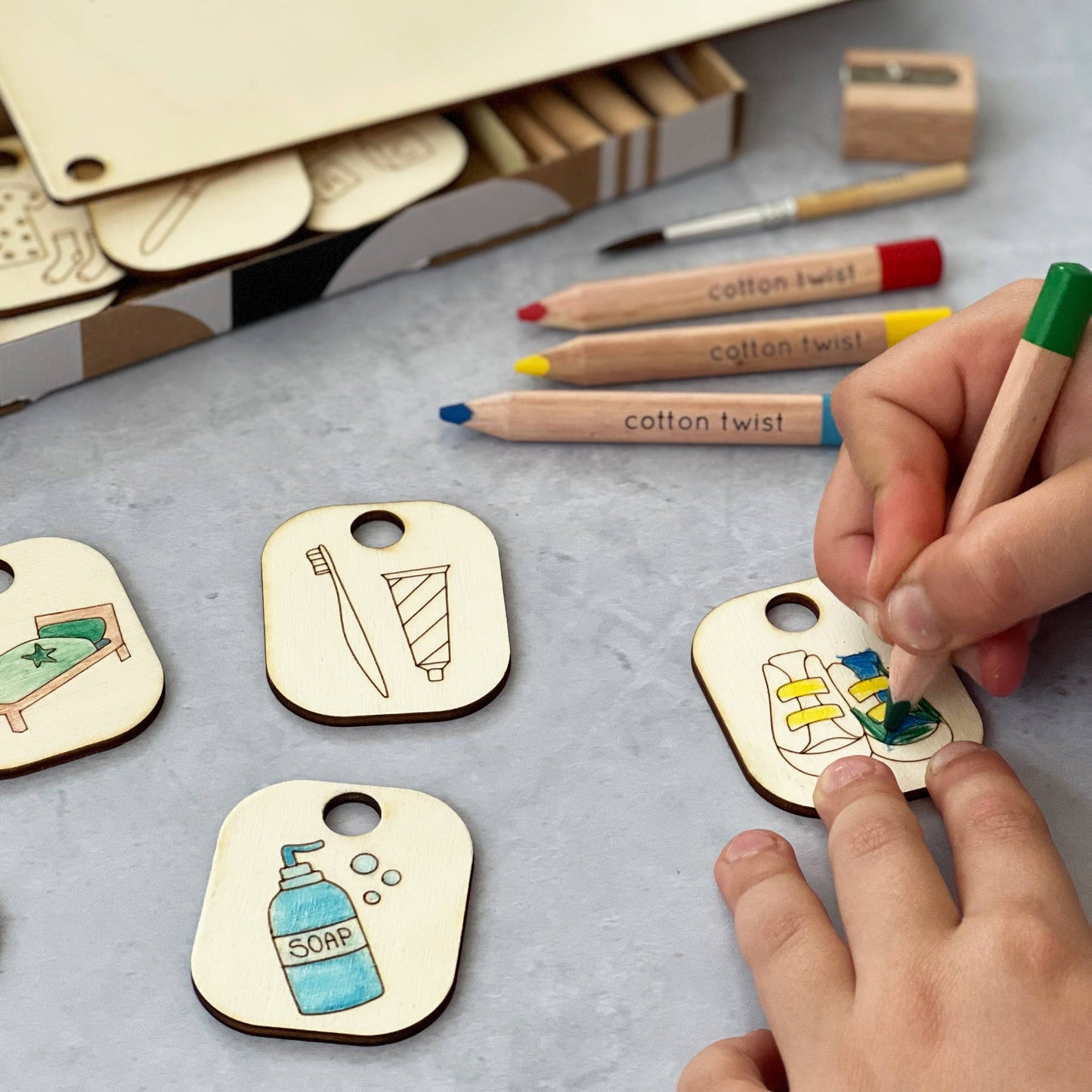 The wooden Daily Task Chart display stand holding four hand-colored chore tokens: putting on shoes, playing with blocks (or learning), brushing teeth, and a star reward token. The chart is a completed, customized visual aid for a child's routine.